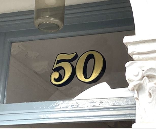 Gold number 50 displayed on a glass window above a doorway frame.