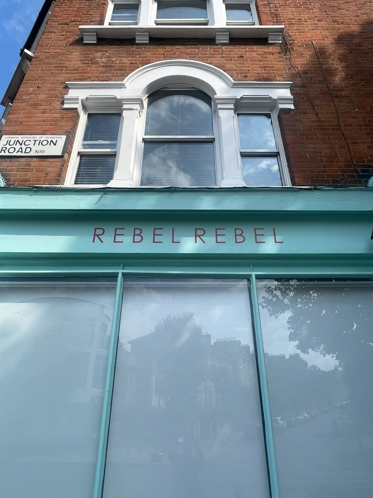 image | NGS Sign lettering & writing. Turquoise storefront with 'REBEL REBEL' sign beneath a brick building.