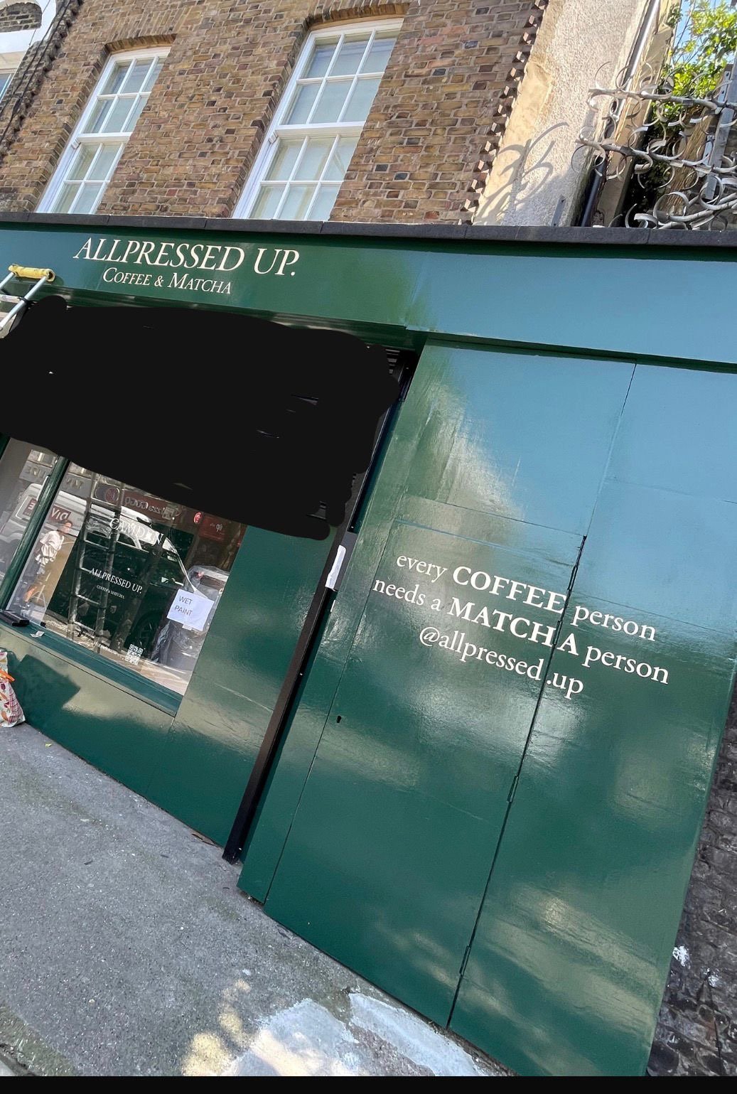 Green storefront for AllPressed Up Coffee & Matcha; door and window visible with brick building above.