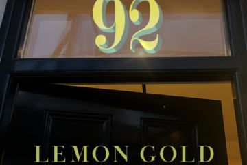 Dark front door with a window above; oversized decorative number '92' centered in the transom, and 'LEMON GOLD' in gold letters across the lower panel.